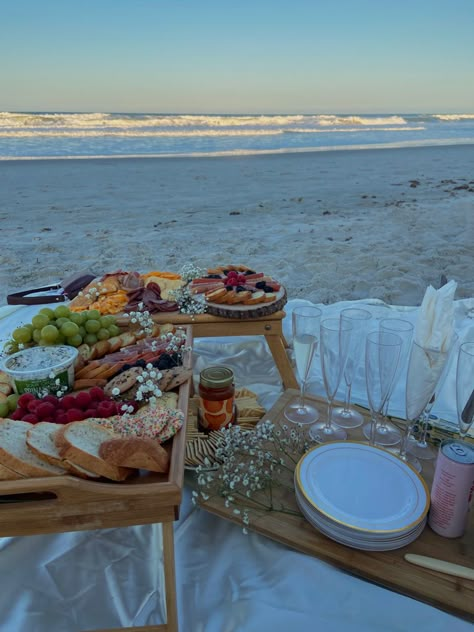 array of 2 charcuterie boards, with a variety of meats, cheeses also seen with flowers, raspberries, blackberries and grapes. aside is champagne flutes with sparkling drinks. all infront of the beach landscape on a sunny spring evening Diy Picnic On The Beach, California Beach Picnic, Beach Picnic Bachelorette Party, Beach Date Picnic, Beach Picnic Bday Party Ideas, Dinner On The Beach Ideas, Cute Beach Picnic Ideas, 21st Birthday At The Beach, Charcuterie Board Beach Picnic