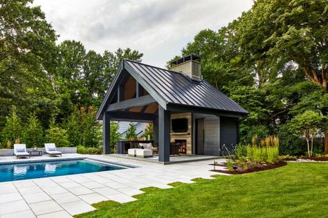 The stone patio of this modern backyard has uneven edges to create visual interest in this modern space. The sleek metal roof is a dark contrast to the custom chimney and fireplace. Pool Pavilion Ideas, Pool House Ideas, Backyard Pool House, Pool House Cabana, Lap Pool Designs, Pool House Design, Backyard Pool Design, Pool Pavilion, Poolside Dining