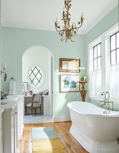 Airy bathroom with pastel green walls, chandelier, soaking tub, sink and cabinets, wall art, large windows, and a desk and chair. Mediterranean Color Palette, Mint Green Paints, Mint Paint, Bathroom Wall Colors, Light Green Walls, Mission Style Homes, Mediterranean Living Room, Mint Green Walls, Mint Walls