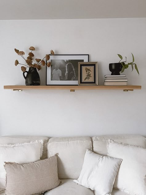 Pictures Above Sectional Couch, Picture Layering On Shelf, Simple Living Room Shelf Decor, Single Shelf Styling Living Room, Wood Wall Shelves Living Room, Shelf With Frames Above Couch, Floating Shelves Living Room Pictures, Above The Couch Shelf Decor, How To Style Floating Shelves Bedroom