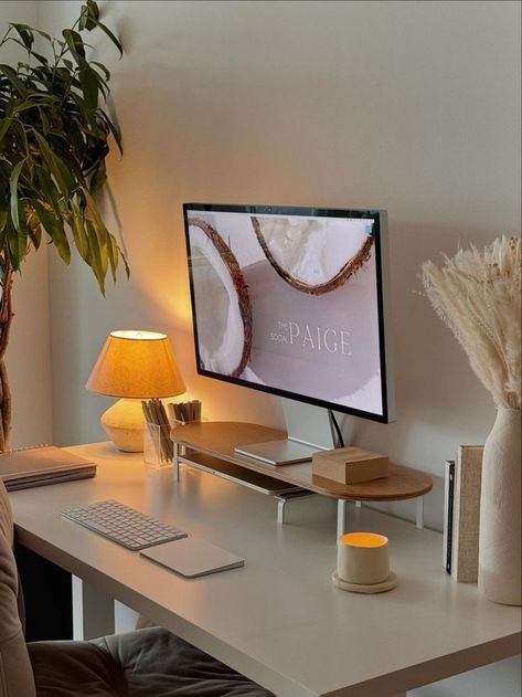 A cozy home office featuring a minimalist desk setup with neutral colors, warm lighting from a small lamp, a wooden monitor stand, and green plant decor, creating an elegant and serene workspace. Cozy Desk, Cozy Home Office, Deco Studio, Desk Inspiration, Aesthetic Space, Warm Lighting, Office Room Decor, Apartment Decor Inspiration, Home Office Setup