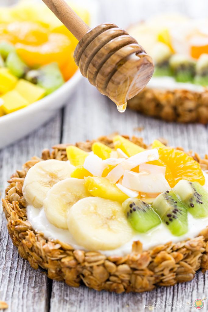 a bowl of fruit salad with a honey dip on top and a plate of fruit in the background