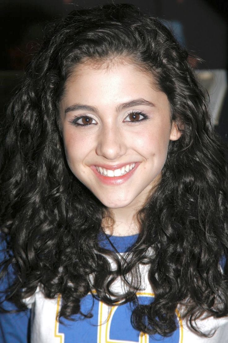 a girl with long curly hair smiling at the camera while wearing a blue and white shirt