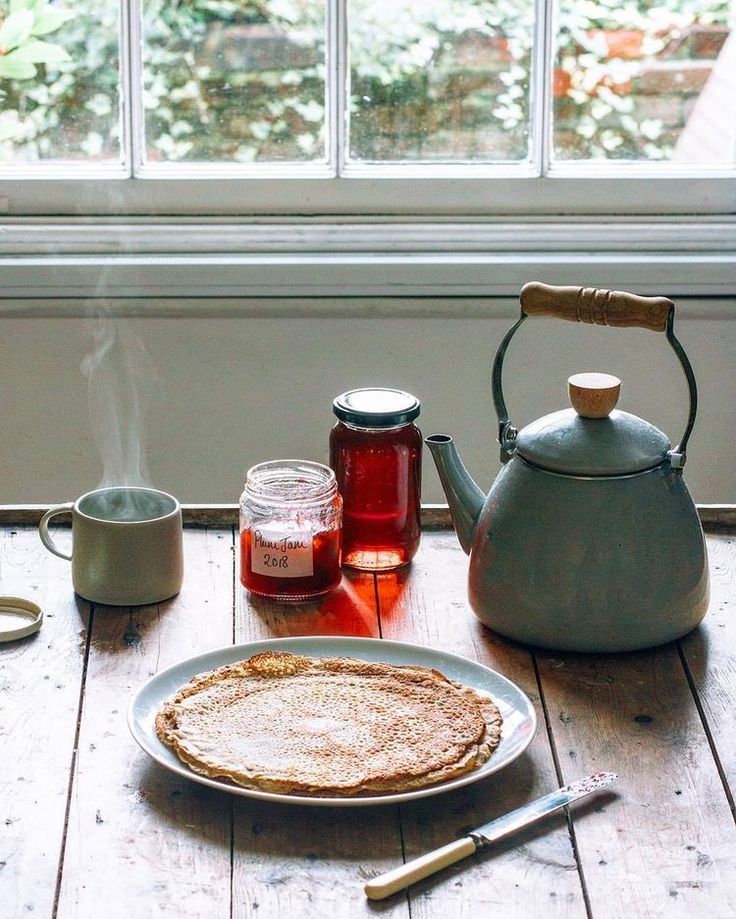 a pancake on a plate next to a tea kettle and cup with liquid in it