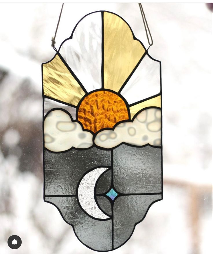 a stained glass sun catcher hanging from a window with the moon and clouds on it