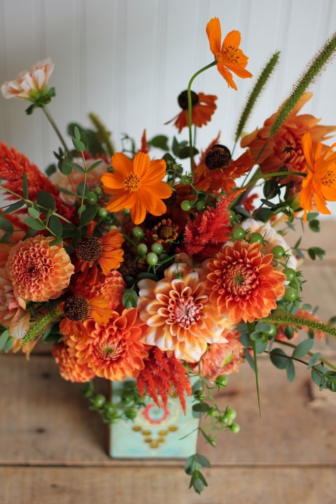 a vase filled with orange and red flowers on top of a wooden table next to a wall