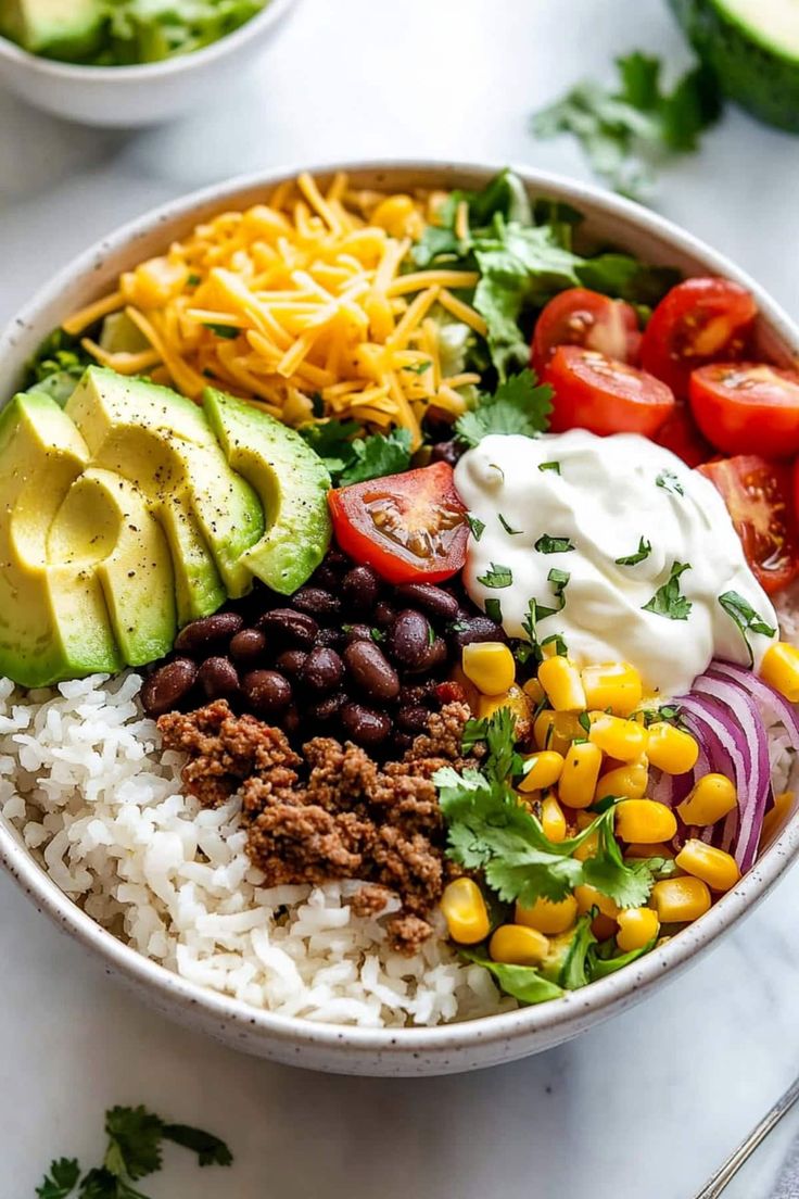 a white bowl filled with rice, beans, avocado, corn and tomatoes