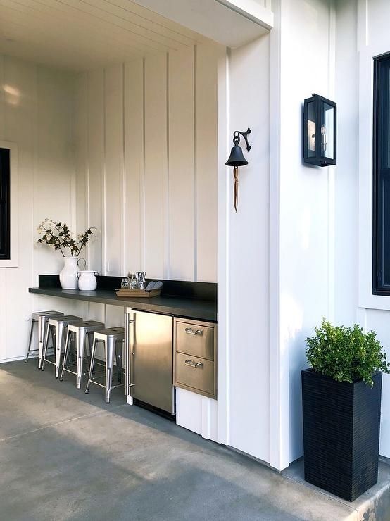 an outdoor kitchen with stainless steel appliances and bar stools next to the house's front door