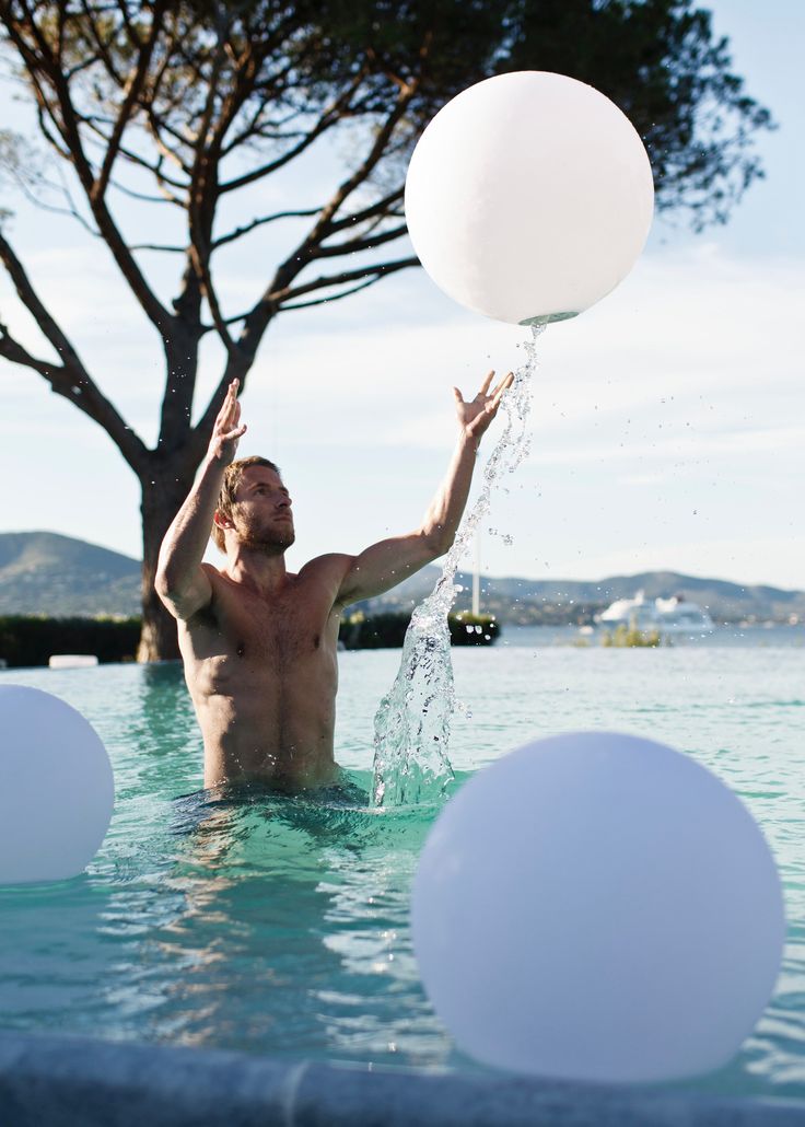 a man is in the water playing with some white balloons while holding up a large white balloon