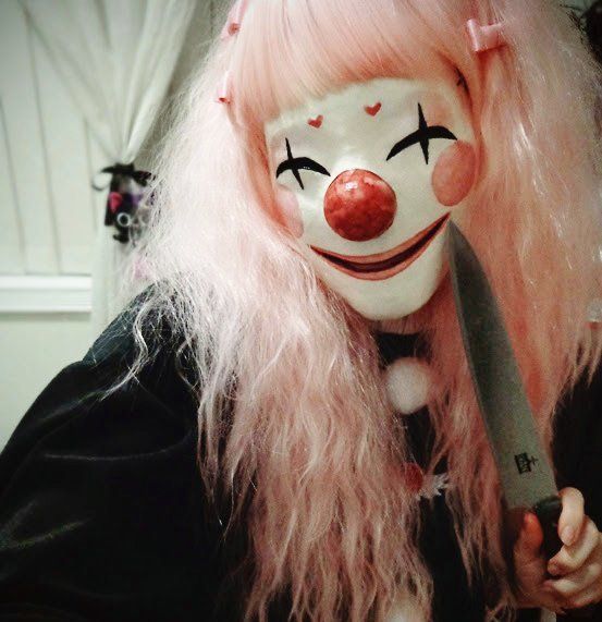 a woman with pink hair and clown makeup holding a knife in front of her face