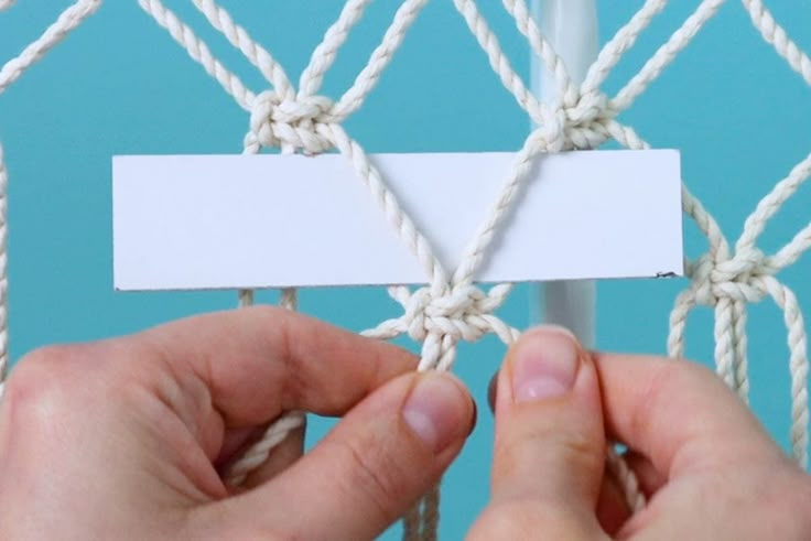 two hands holding a piece of white paper over a roped net with blue background