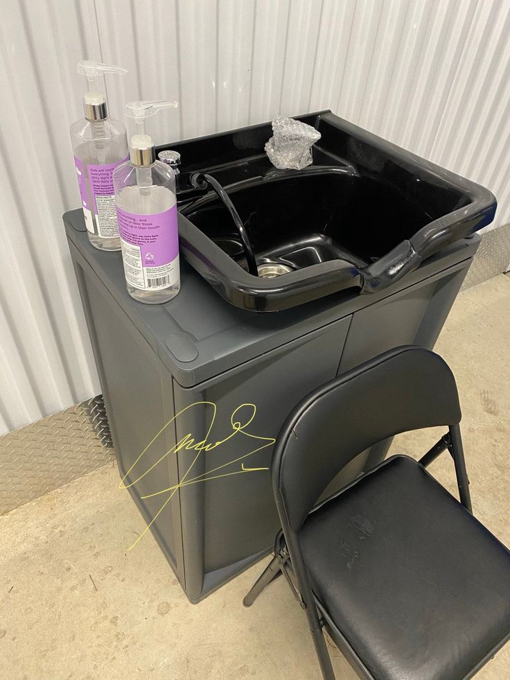 a black chair sitting next to a cooler with bottles on it and soap in the tub