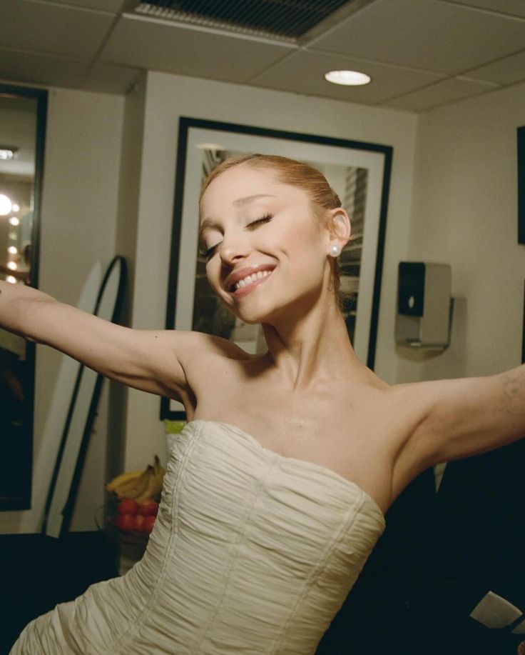 a woman in a strapless white dress is smiling and stretching her arms out to the side