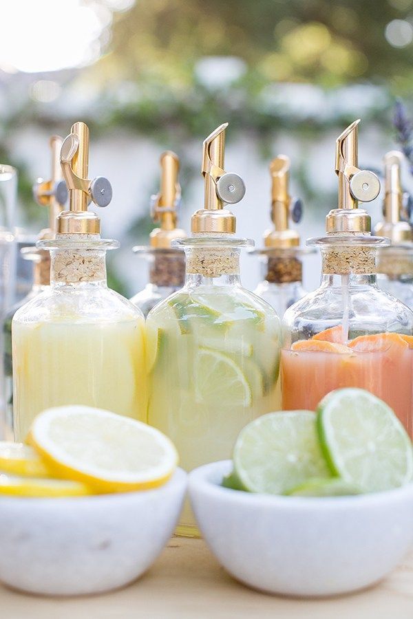 bottles filled with different types of drinks on top of a wooden table next to lemons and lime wedges