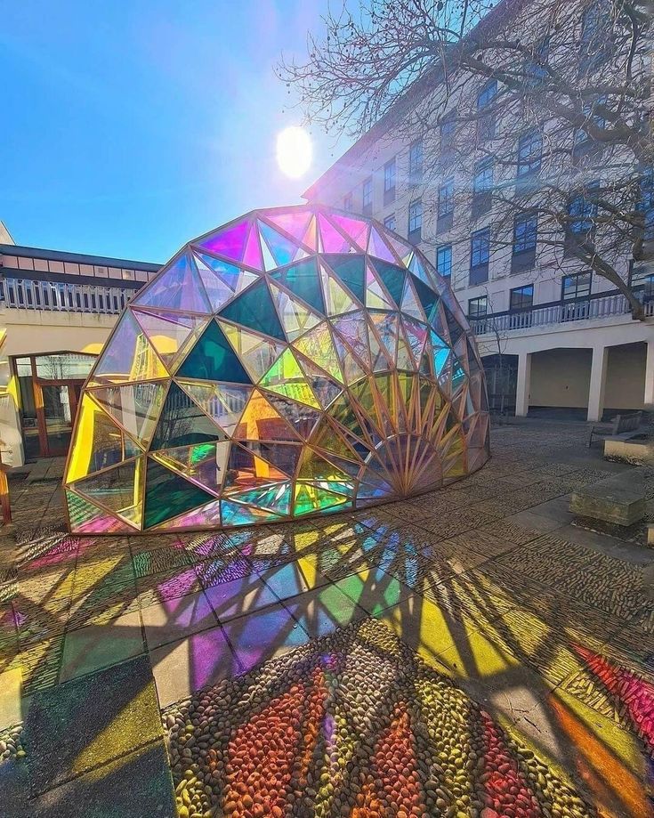 the sun shines brightly on an art installation in front of a building with multiple colored glass structures