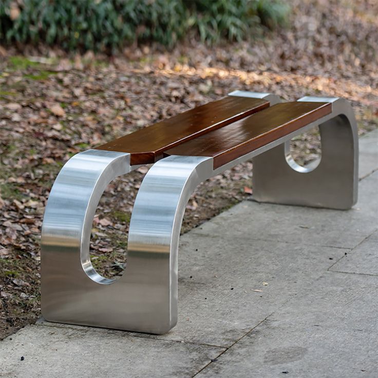 a metal and wood bench sitting on the side of a sidewalk in front of some leaves