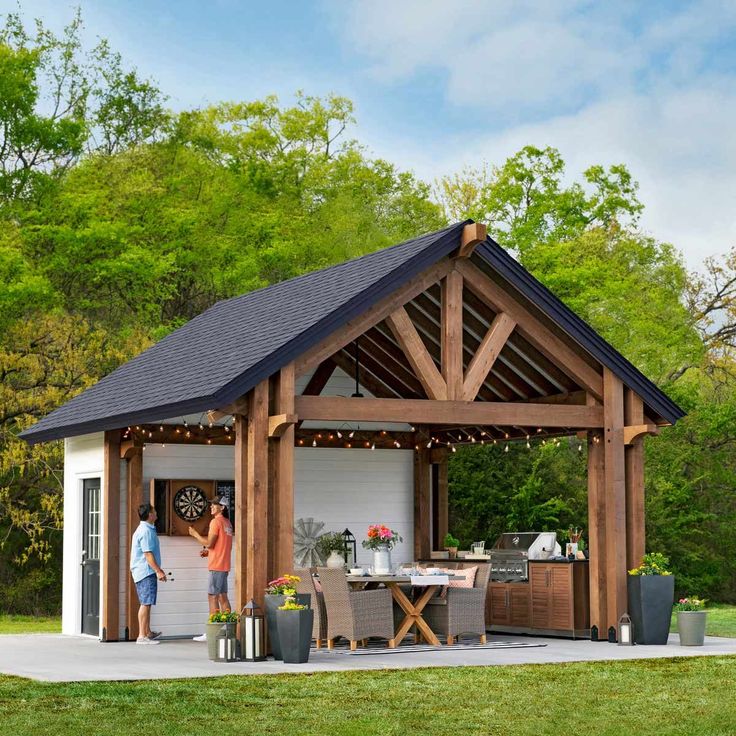 two people are standing in front of a shed with an outdoor kitchen and dining area