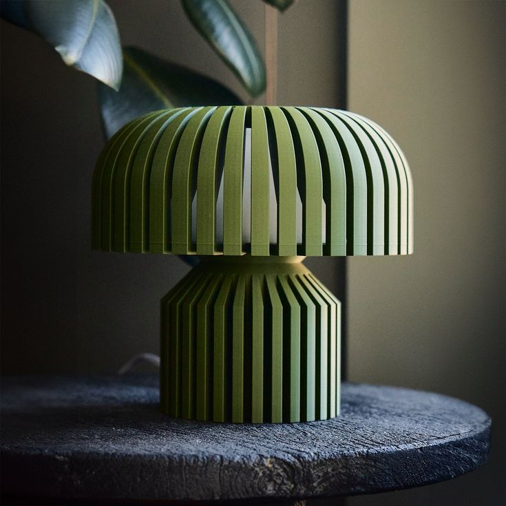 a green striped lamp sitting on top of a table next to a potted plant