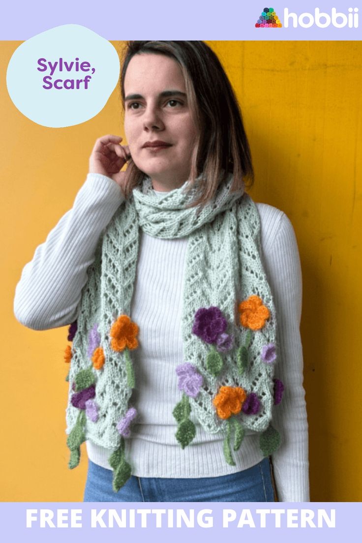 a woman standing next to a yellow wall wearing a green scarf with flowers on it