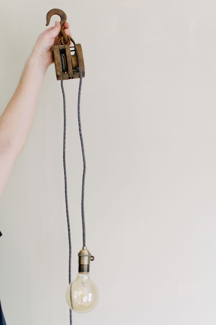 a person holding an old fashioned light bulb in front of a white wall with a wrench hanging from it