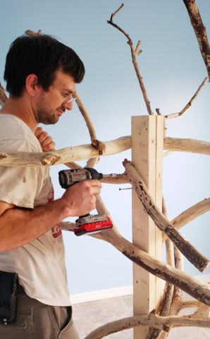 a man is using a drill to fix a piece of wood that has been made from branches