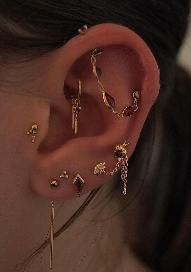 a woman wearing gold ear piercings with different types of jewelry on her left ear