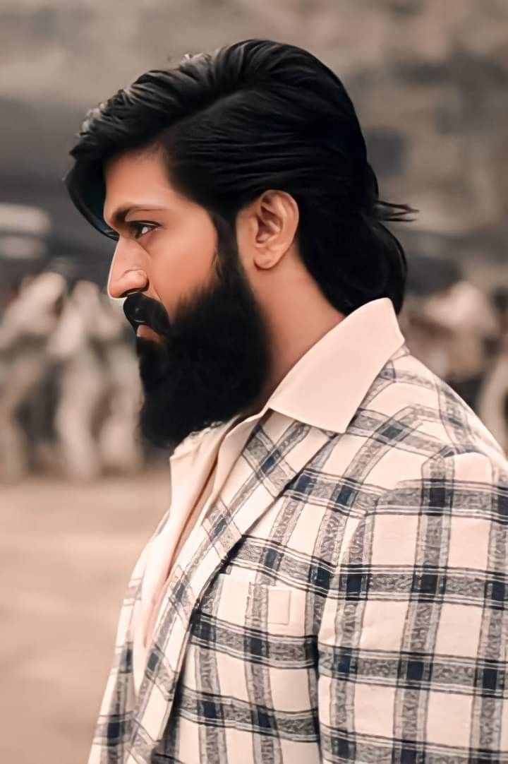 a man with black hair and beard standing in front of cows wearing a checkered shirt