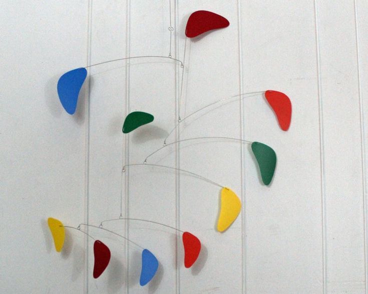 a colorful wind chime hanging from the side of a white wall with red, green, yellow and blue colors