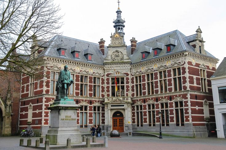 an old building with a statue in front of it and people walking around the courtyard