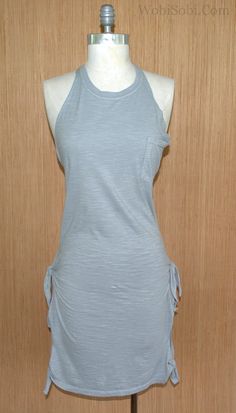 a mannequin wearing a gray dress on a wooden stand in front of a wall