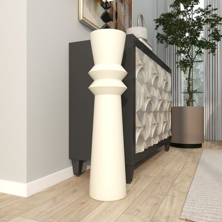 a tall white vase sitting on top of a hard wood floor next to a wall