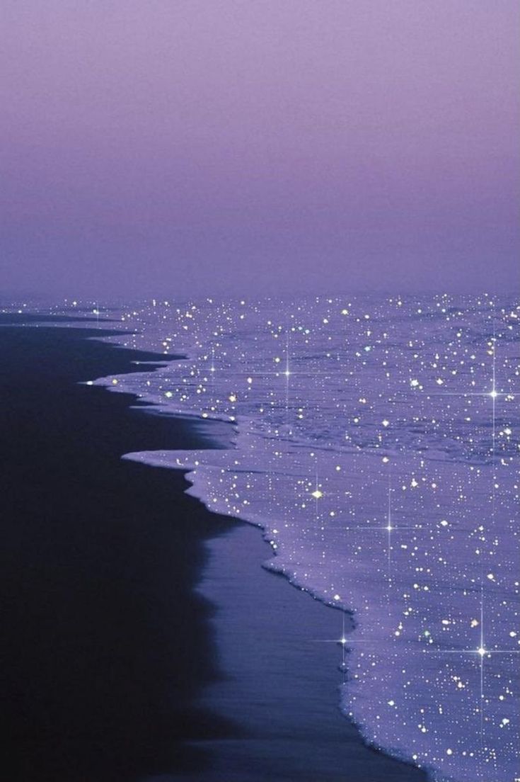 the beach is lined with sparkling lights and stars in the sky at night, as seen from an airplane