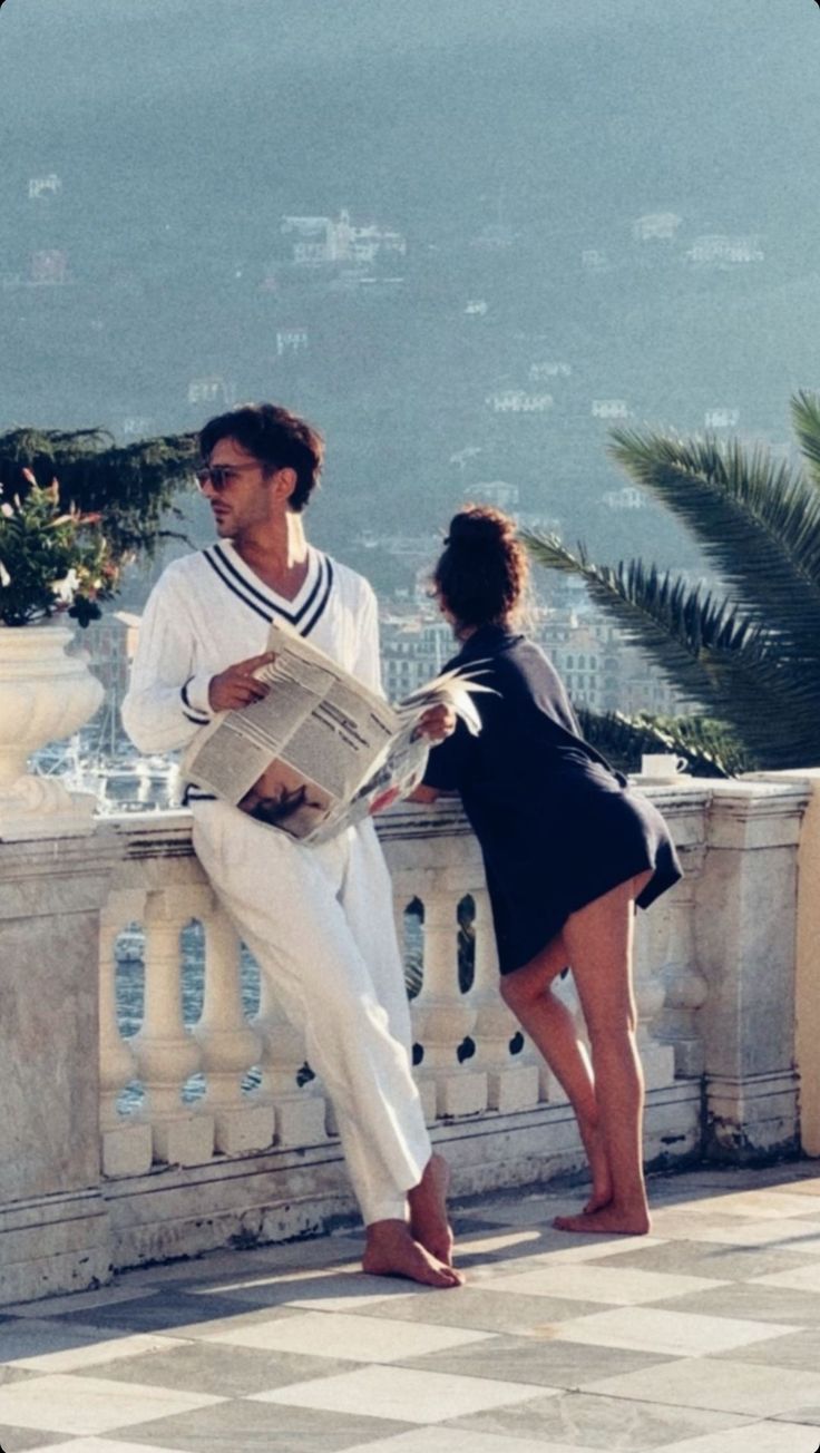 a man and woman standing next to each other on a balcony with the ocean in the background