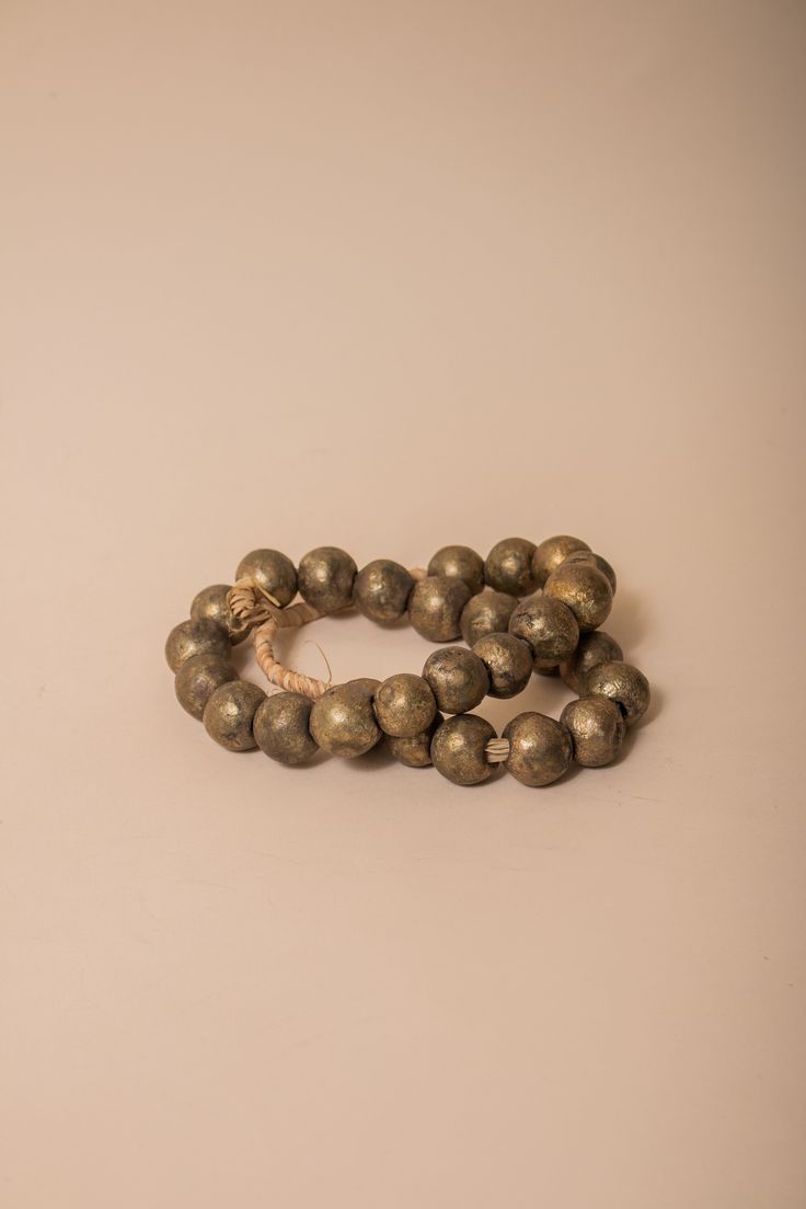 These brass African beads are beautifully textured, each individual bead unique in shape and finish for a final look that feels one-of-a-kind and natural. Perfect for layering on a vase, an open book, a bowl, or styling on a shelf. All Sales Final Free Shipping Artisan Gold Bracelets With Wooden Beads, Gold Beaded Bracelets With Wooden Beads, Bronze Jewelry With Wooden Beads For Gift, Unique Gold Beaded Bracelet With Wooden Beads, Unique Gold Beaded Bracelets With Wooden Beads, Bronze Jewelry With Large Beads, Brass Beaded Bracelets With Round Beads, Traditional Gold Beaded Bracelets With Wooden Beads, Rustic Round Beads Jewelry For Meditation