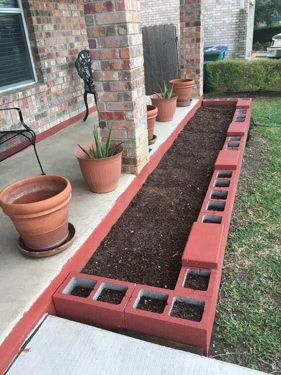 an empty garden bed in front of a brick house with potted plants on the side