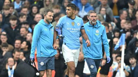 Rodri is helped from the pitch by Manchester City medical staff