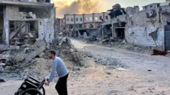 Columns of smoke rise behind a man pushing a wheelchair after the Israeli shelling of Beit Lahia in the northern Gaza Strip 