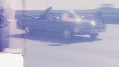 JFK's presidential limousine speeding down the street, a Secret Service agent is on the side