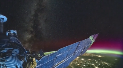 ISS orbiting over globe with green and purple lights shining over Earth