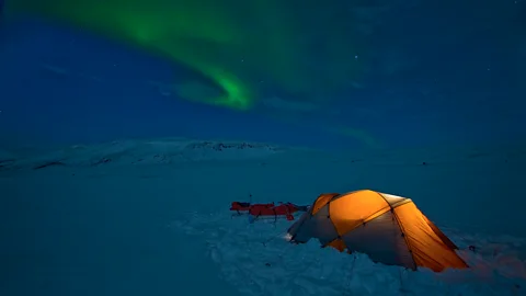 Getty Images An illuminated tent in a dark snowy landscape with the Northern Lights above (Credit: Getty Images)