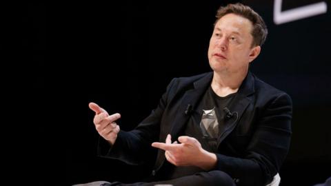 Elon Musk talking at a conference wearing a blue jacket