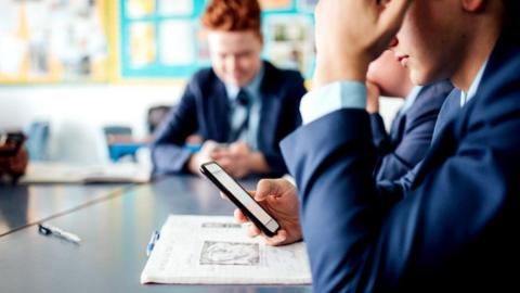 Schoolboy holding a mobile phone in classroom