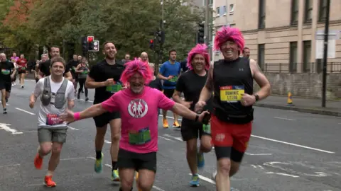 Three male runners wearing bright pink smile at the camera.