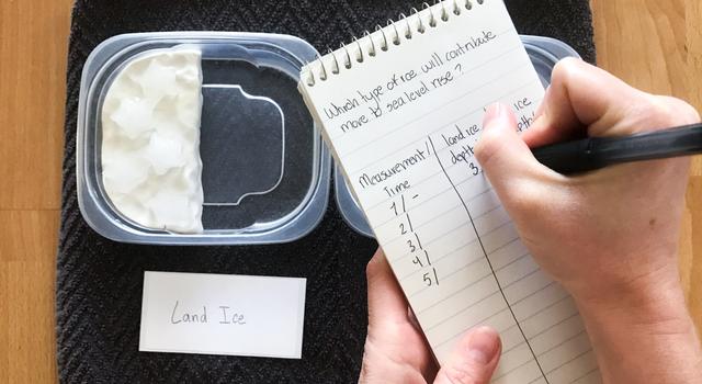 A person writes down measurements on a notepad above their ice melt experiment