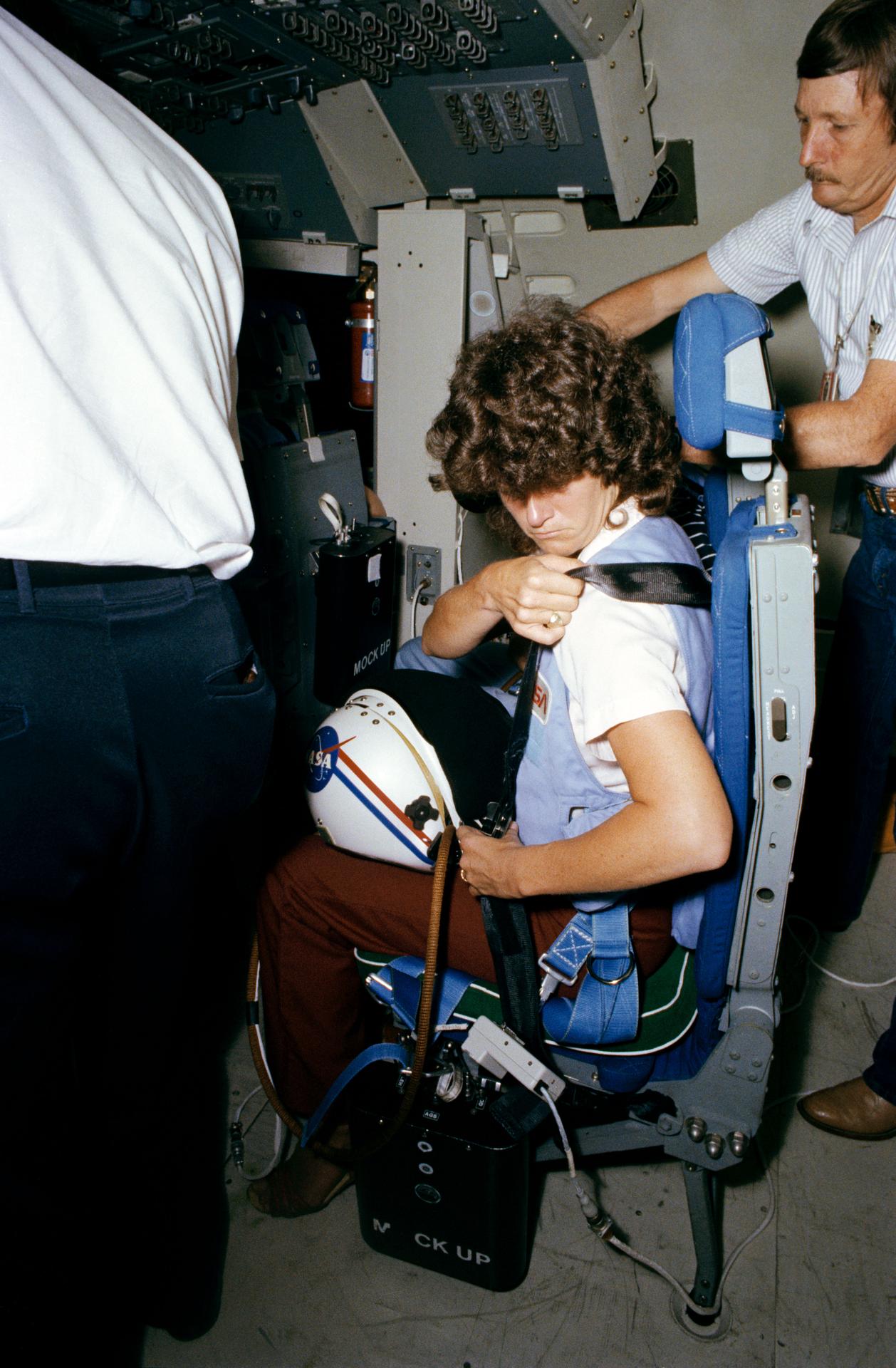 A woman adjusting a strap on a space shuttle seat during training.