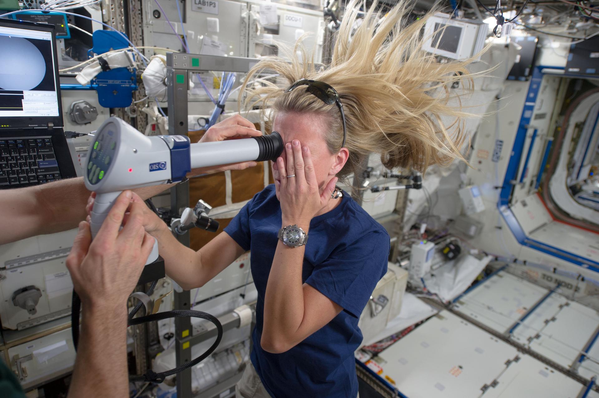 Astronaut Karen Nyberg and Astronaut Chris Cassidy (partially visible), both Expedition 37 flight engineers, perform an Ocular Health (OH) Fundoscope Exam in the Destiny laboratory of the International Space Station