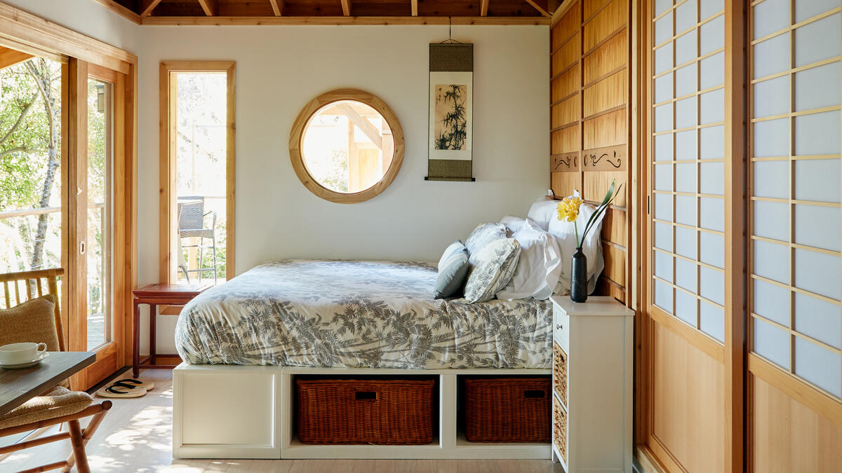 Ett sovrum med ett cirkulärt fönster på väggen och en gul blomma i en vas på nattduksbordet.