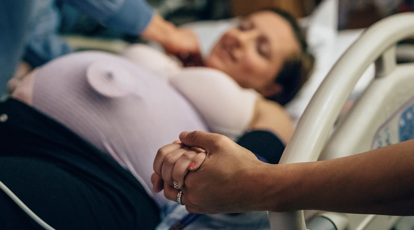 couple holding hands while woman is in labor in hospital bed