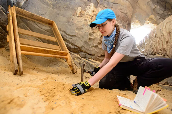 Photo of student in the field with archealogical tools