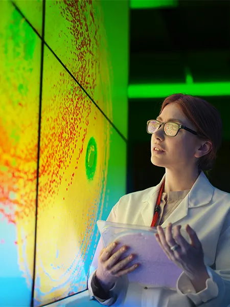 Researcher looking at colorful graphic on large screen while holding a device